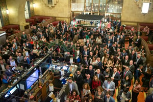 Large indoor gathering at a former brewery space inside Los Angeles Union Station. Hundreds of people are present, all dressed in business attire such as suits, dress shirts, and professional outfits. The crowd is densely packed and collectively facing upward toward the camera’s vantage point, creating a sense of scale and engagement. The space has an industrial feel consistent with a repurposed brewery venue, with high ceilings and open floor area. The overall atmosphere suggests a formal or corporate event taking place in a historic transit-adjacent setting.