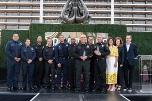 A group of Los Angeles Fire Department members stands on stage at the Central City Association’s “Treasures of Los Angeles” event, gathered around former Chief Villanueva and CCA CEO Nella McOsker at center. The individuals are dressed in a mix of formal attire and fire department uniforms, facing the audience and standing close together. The stage setting and lighting highlight the group as part of their recognition during the program.