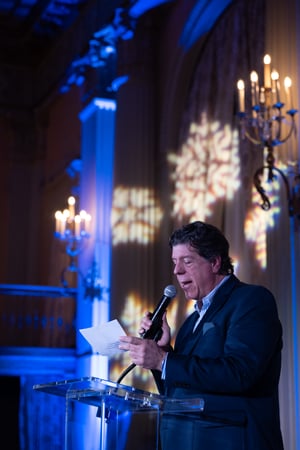 A man speaks from the podium as guests gather and celebrate at the Central City Association’s holiday party, socializing in a festive indoor setting with warm lighting and seasonal décor.